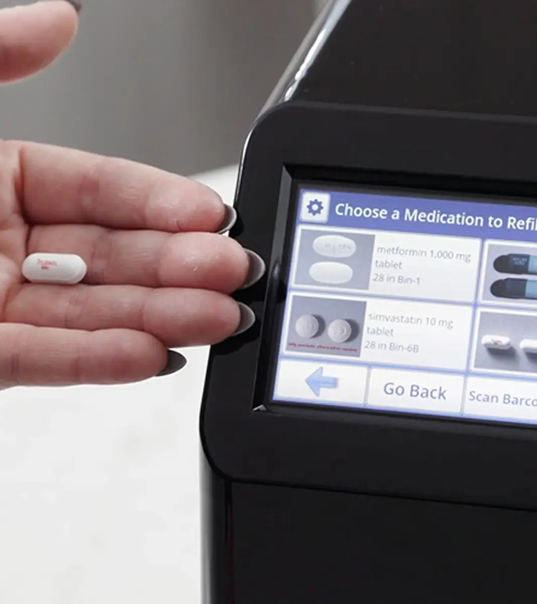 Hand holding a pill next to Medacube Automatic Pill Dispenser Screen