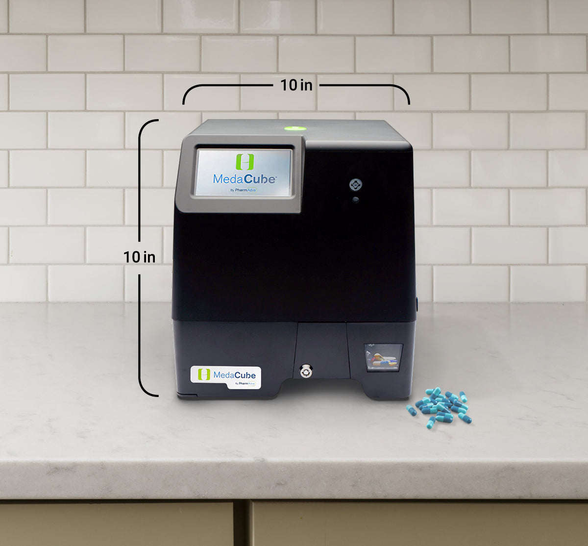 MedaCube device on counter with 10 inch measurement  and 10 inch measurement across the width of the device and a 10 inch measurement on the left side of the device showing the height. Pills on counter.