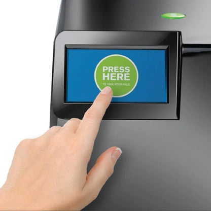 Shows a finger pressing the touch screen on the MedaCube. The screen shows a press here button showing that medications are ready to take. 